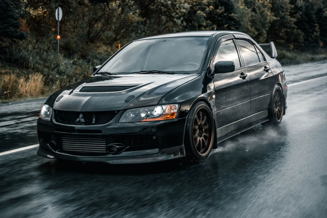 A black car speeds on a wet road, showcasing its design and speed in an outdoor setting.
